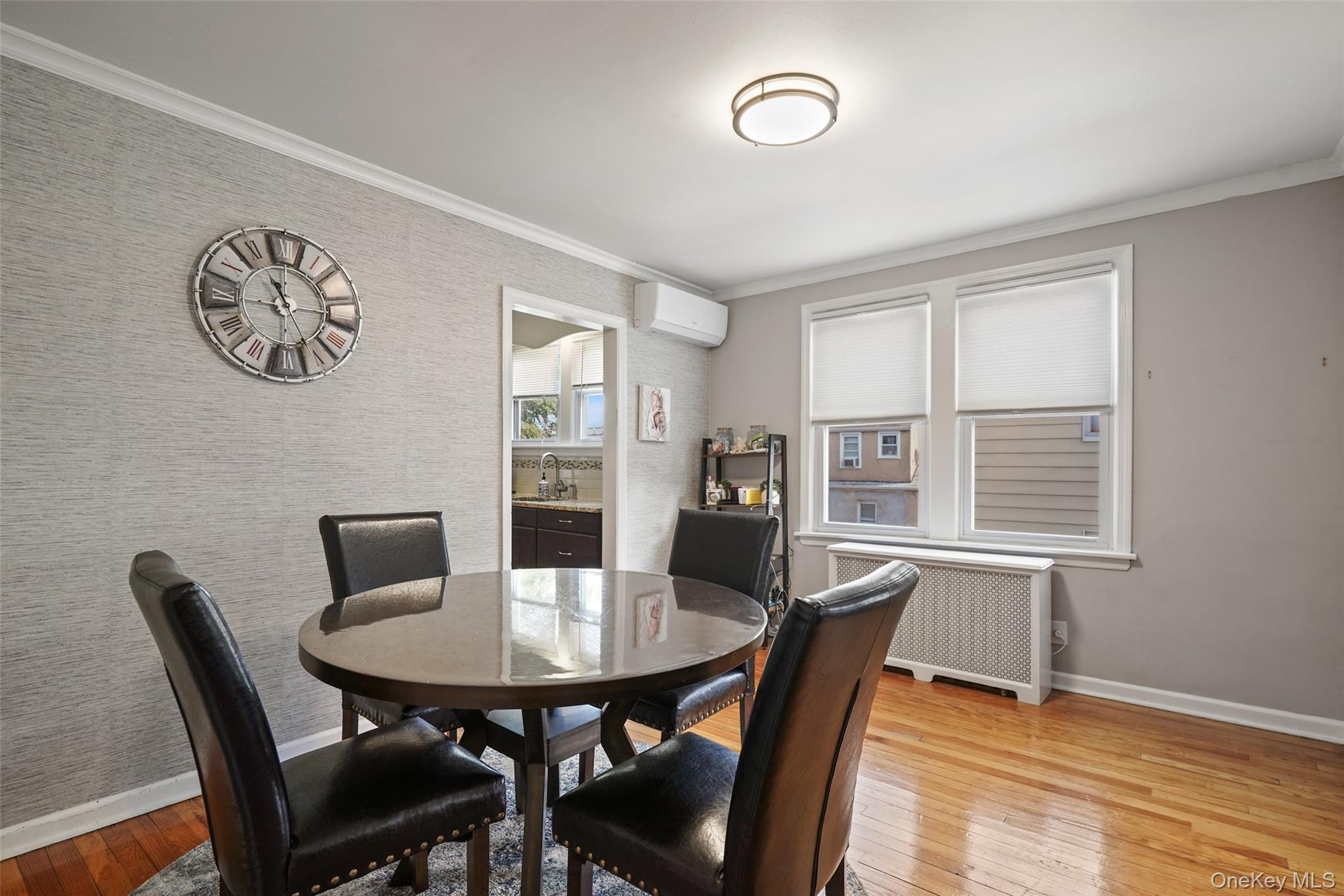 Dining room with a round glass-top table, dark leather chairs, hardwood floors, and two windows.