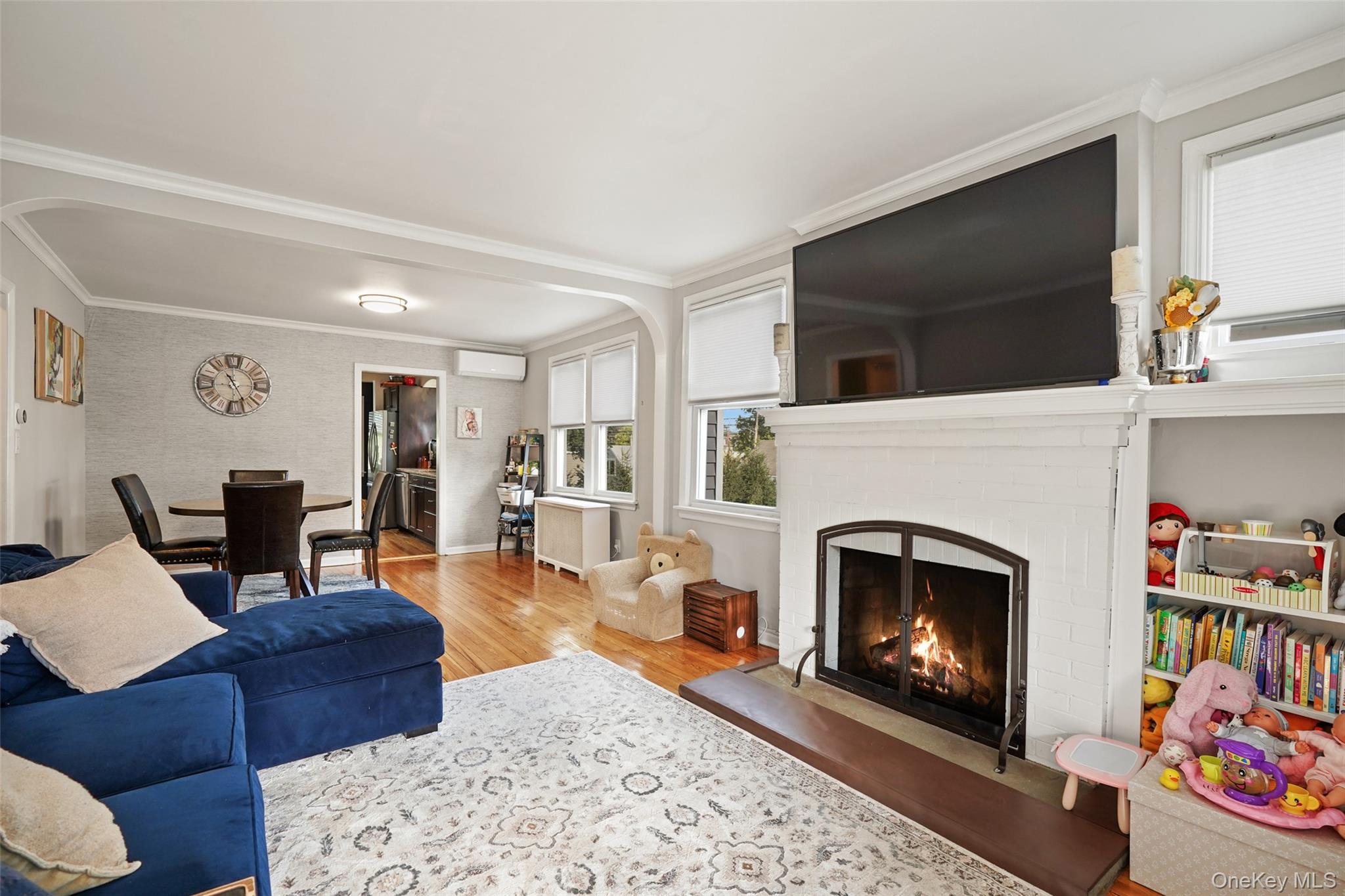 Living room with a blue sectional sofa, patterned rug, and lit fireplace beneath a large television.