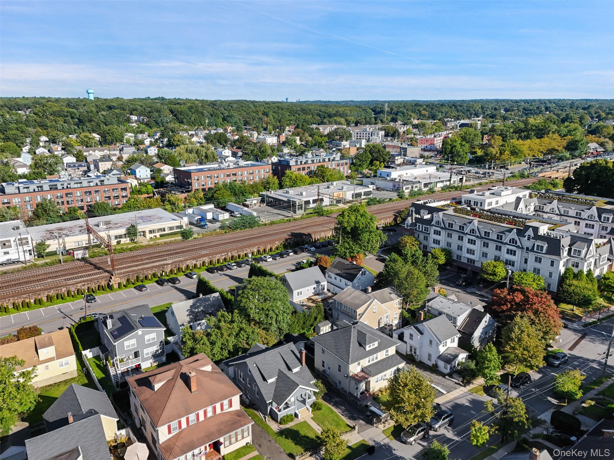 Aerial neighborhood view with homes, railroad tracks, and commercial buildings in the distance.