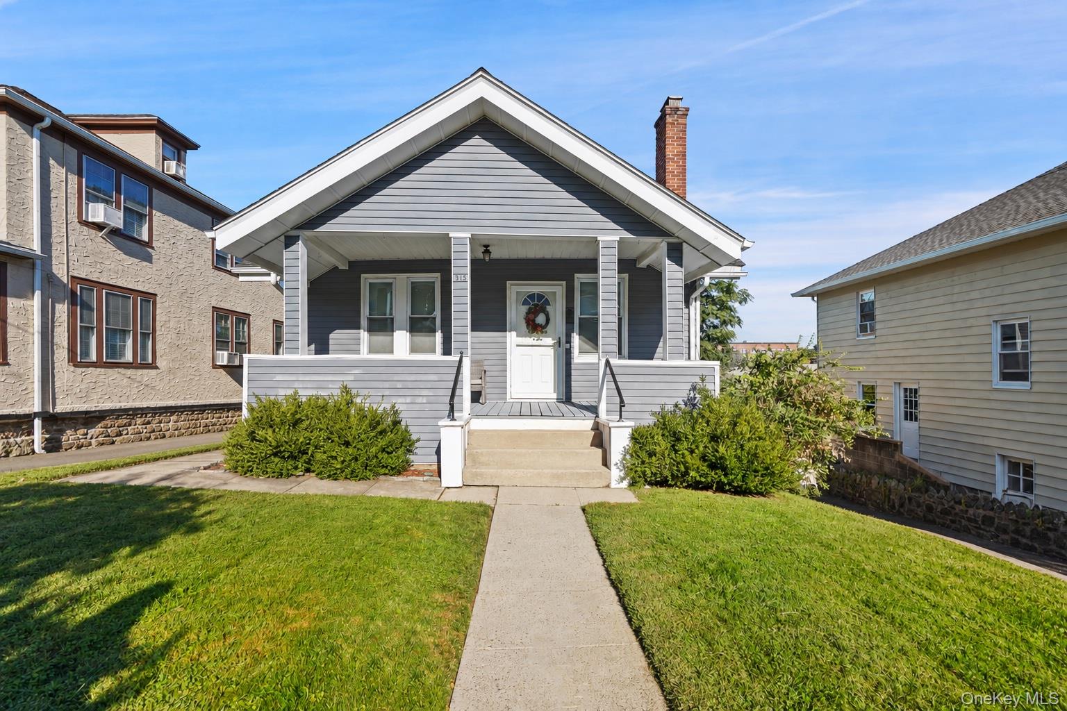 Gray house with a covered front porch, white trim, and a walkway through the lawn.