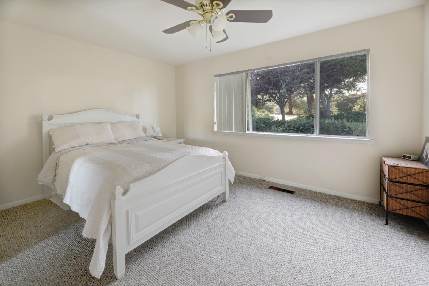 Bedroom with a white bed and wide window overlooking trees and shrubs.