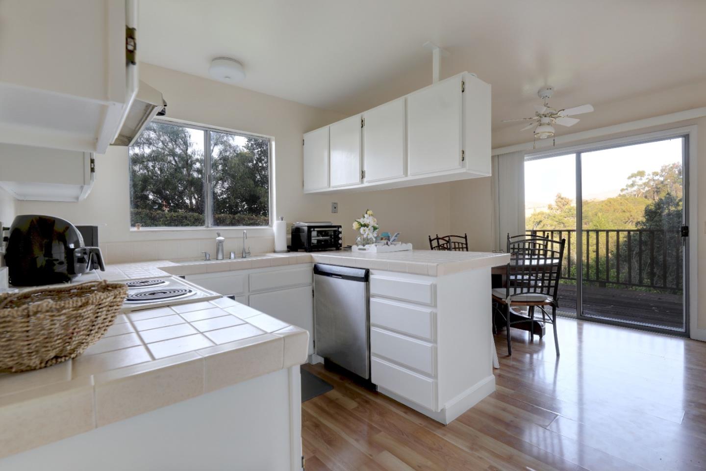 Kitchen with white cabinets and tiled counters, opening to a deck through sliding glass doors.