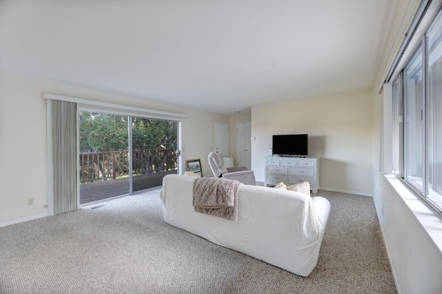 Living room with a white sofa, large windows, and sliding doors to a tree-lined deck.