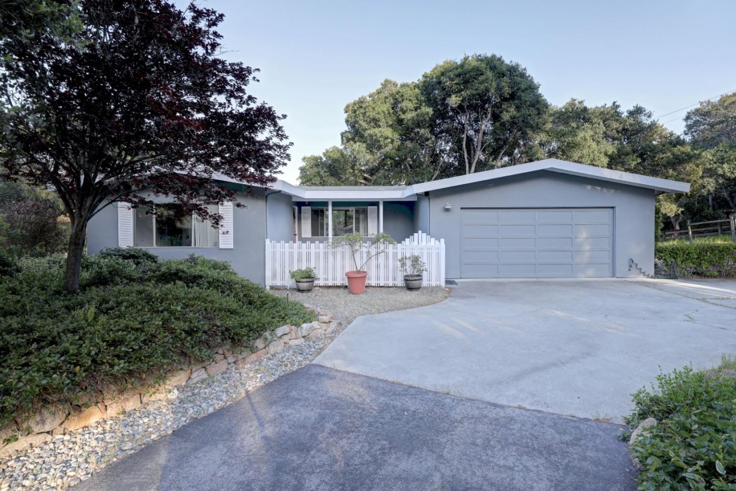 Single-story home with an attached garage, broad driveway, and small white picket fence.