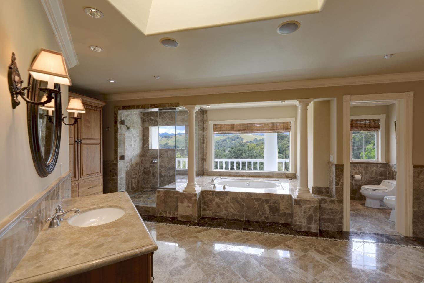 Marble bathroom with a glass shower, soaking tub beneath a large window, and stone vanity.