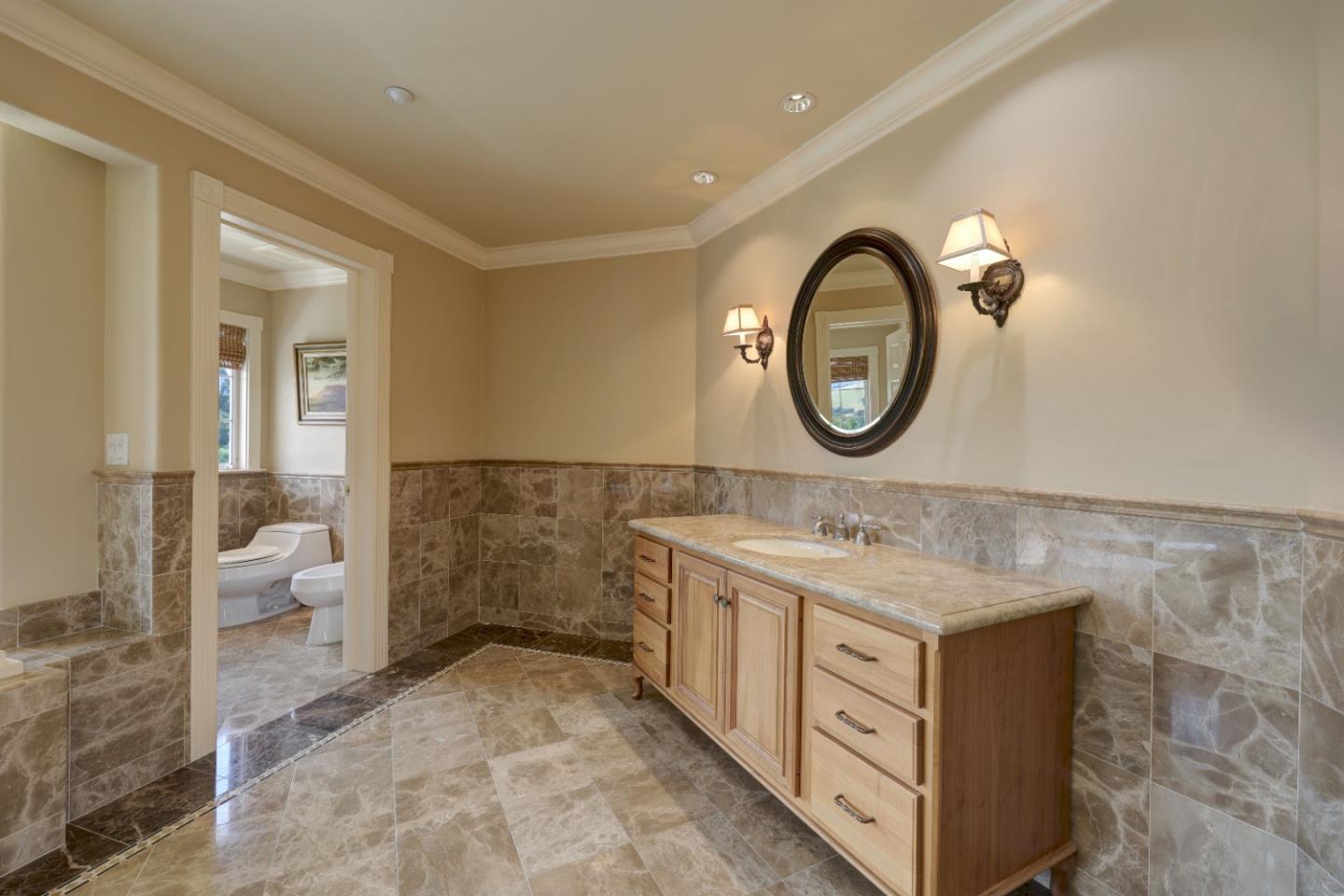 Bathroom with a wood vanity and oval mirror, marble-pattern tile, and an adjoining toilet room.