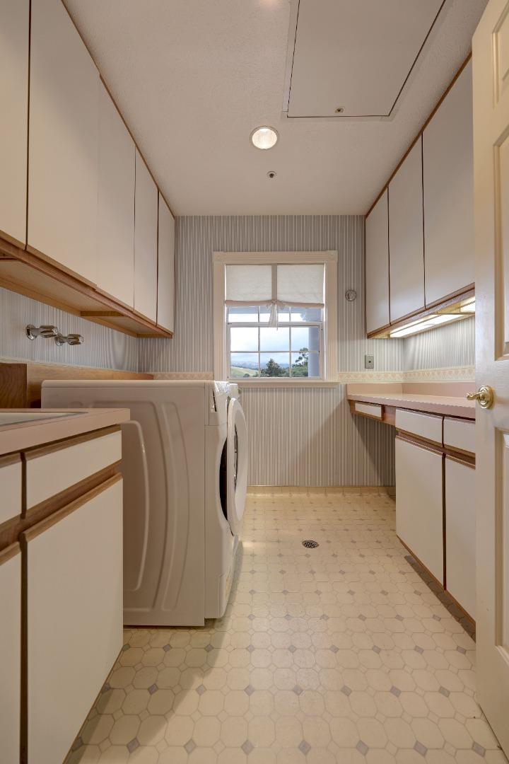 Laundry room with a washer and dryer, built-in cabinets, patterned tile floor, and a window overlooking trees.
