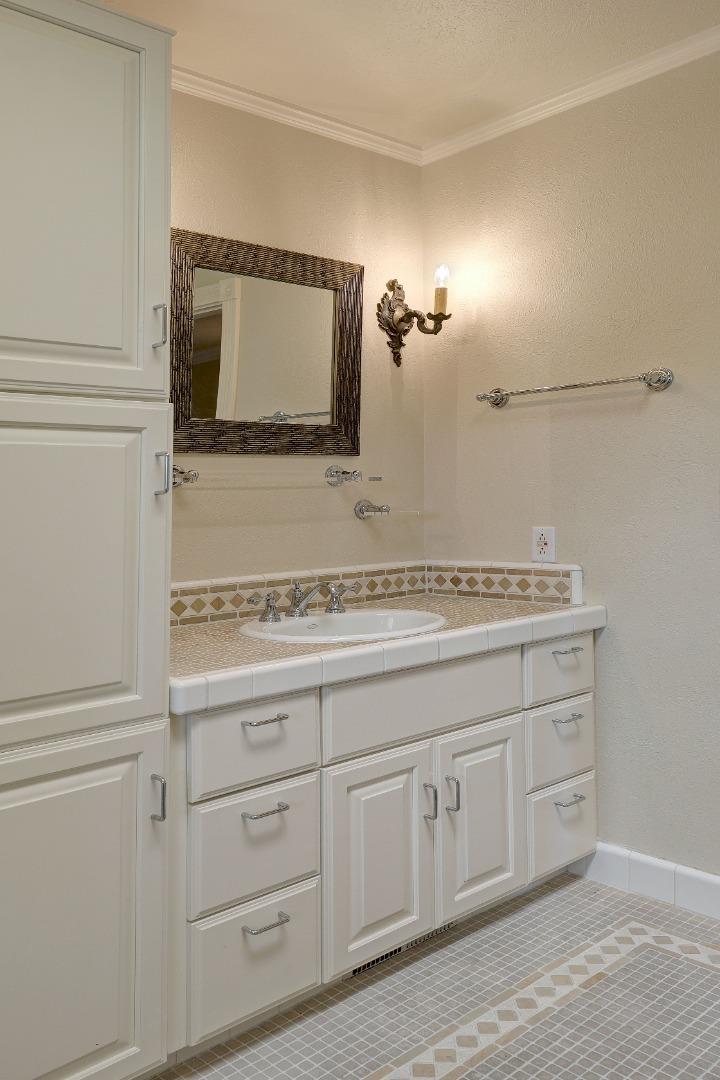 Bathroom vanity with white cabinetry, a tiled counter, framed mirror, and patterned floor.