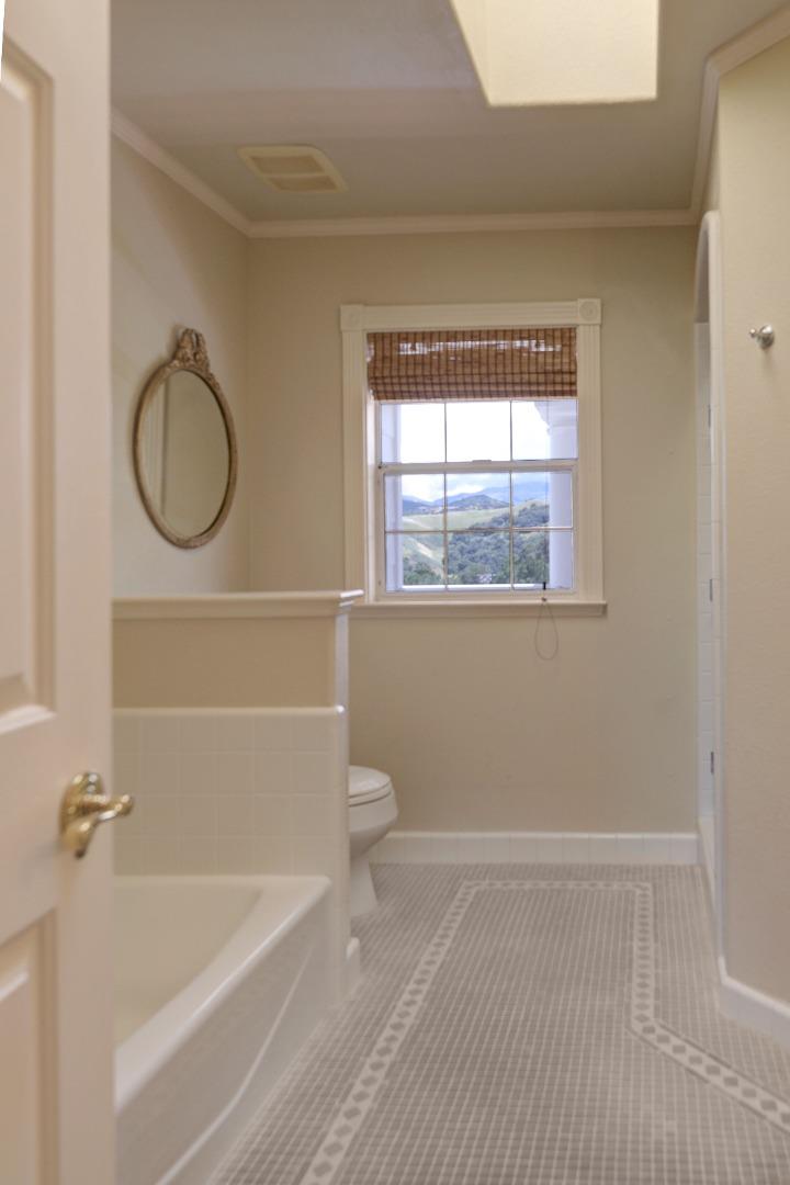 Bathroom with a tiled floor, bathtub, and window overlooking green hills.