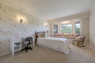 Bedroom with a white bed, floral wallpaper, and large windows overlooking greenery.