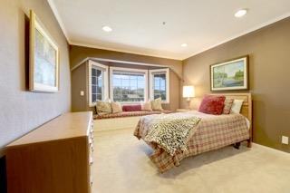 Bedroom with patterned bedding, a bay window and window seat, and a wooden dresser.