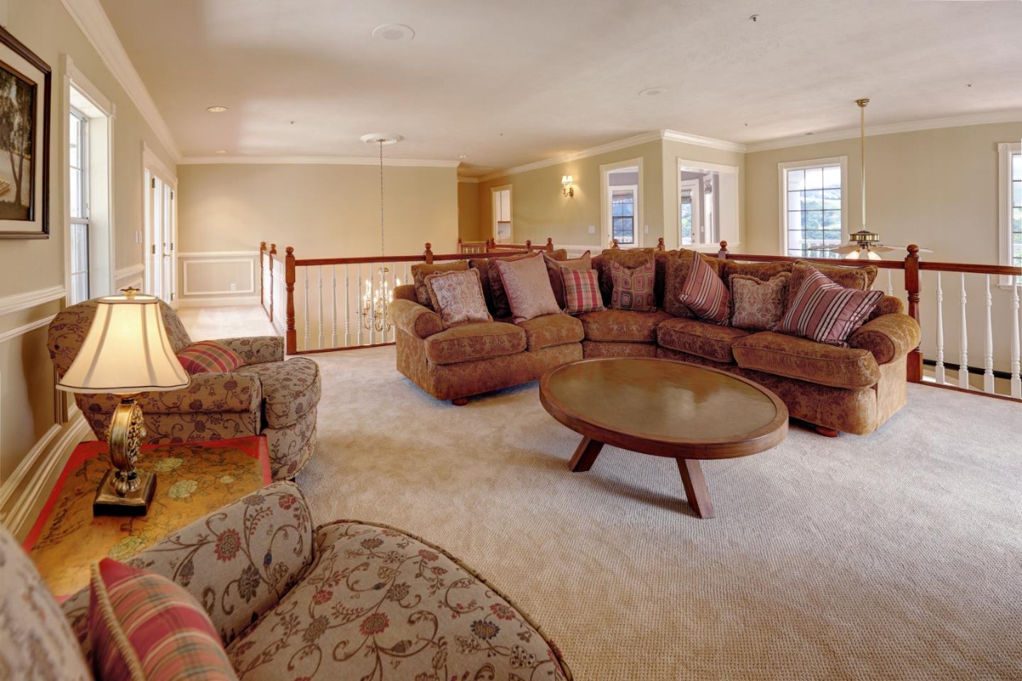Furnished living room with a large brown sectional, patterned armchairs, and a railing around an open stairwell.