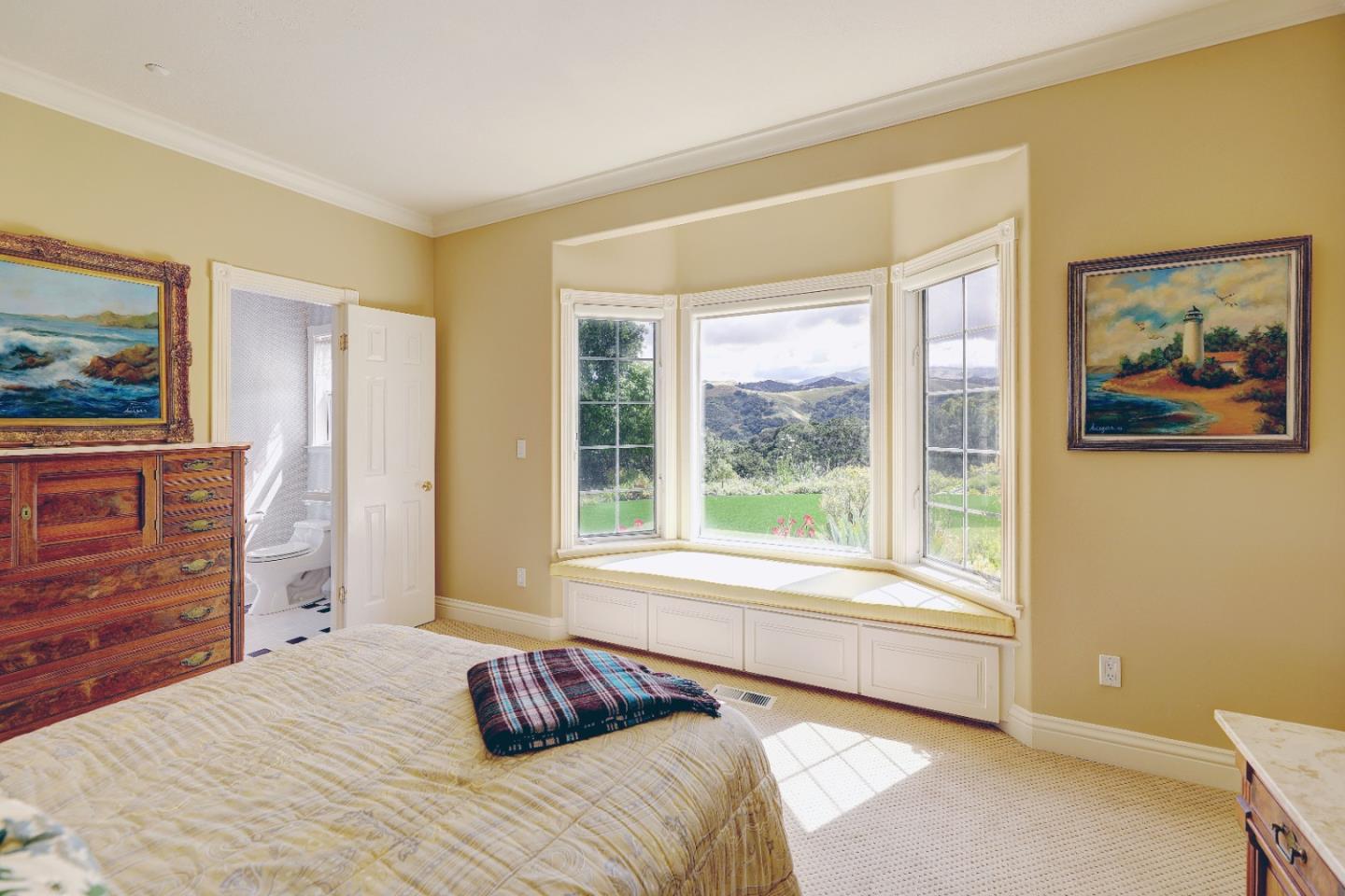 Bedroom with a broad bay window and built-in seat overlooking green hills.