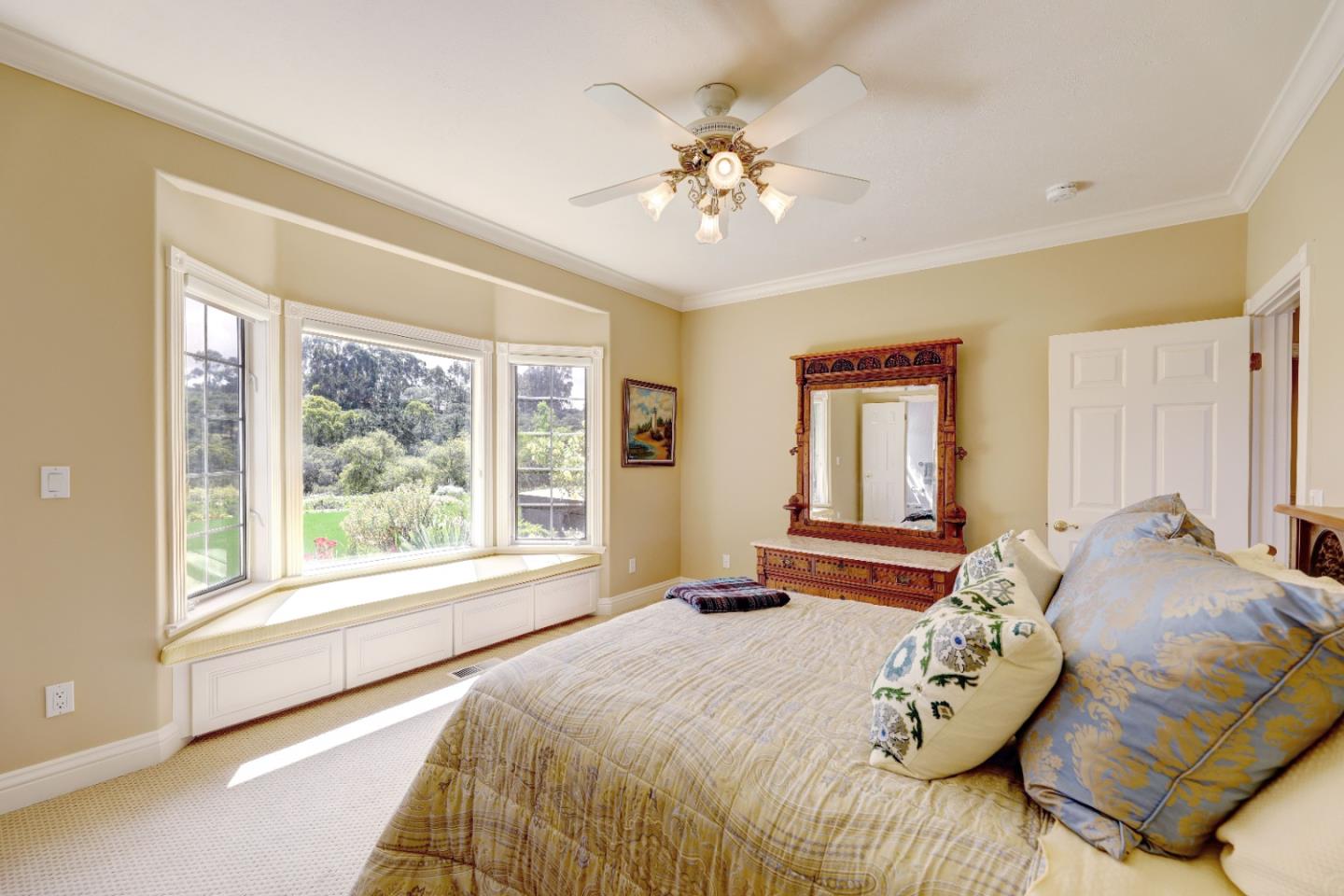 Furnished bedroom with a large bay window, built-in storage, and an ornate wooden dresser and mirror.