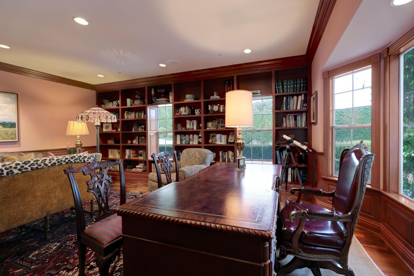 Study with built-in bookshelves, a large wooden desk, leather chairs, and tall windows.