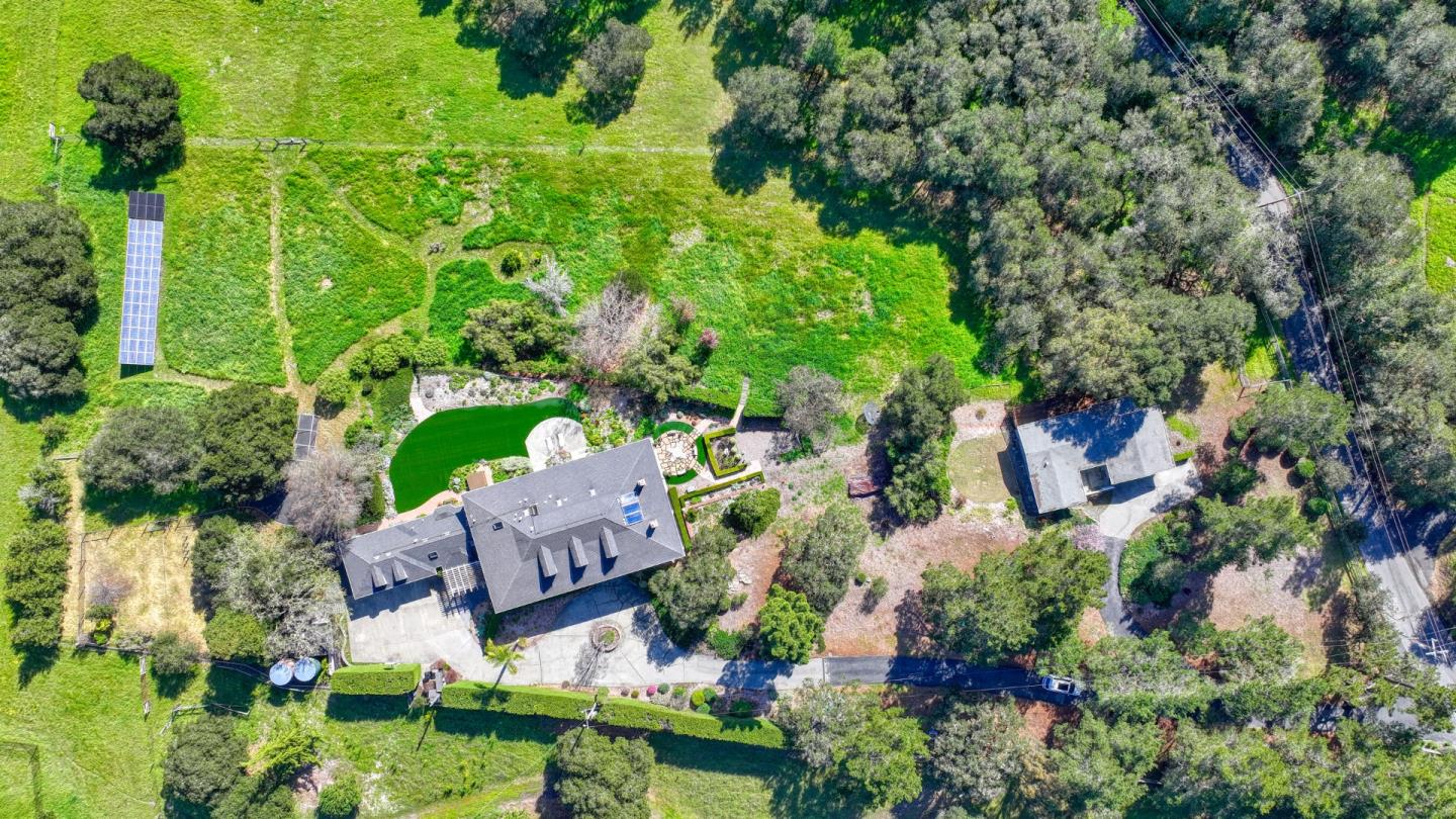 Aerial view of a large home with expansive green grounds, landscaped gardens, solar panels, and a separate outbuilding.