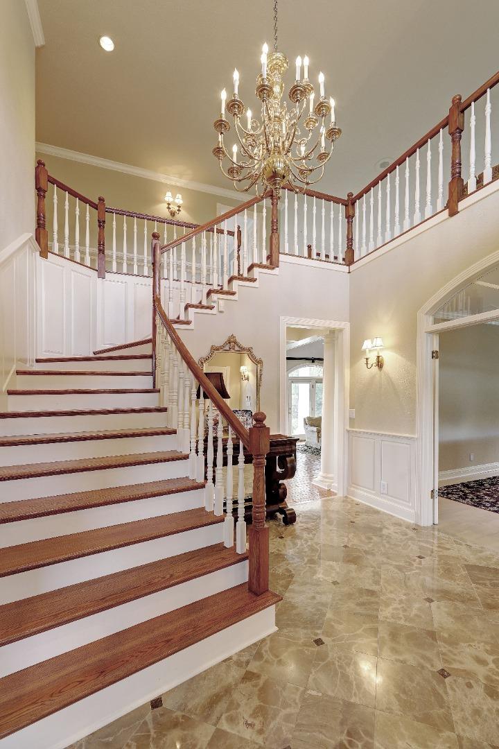 Grand foyer with a sweeping staircase, polished stone floors, and an ornate chandelier.