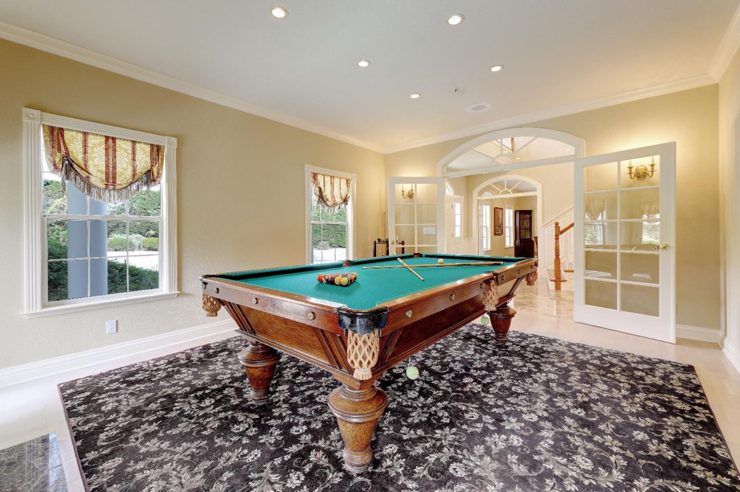 Billiard room with a teal-felt pool table, patterned rug, and glass-paneled doors.