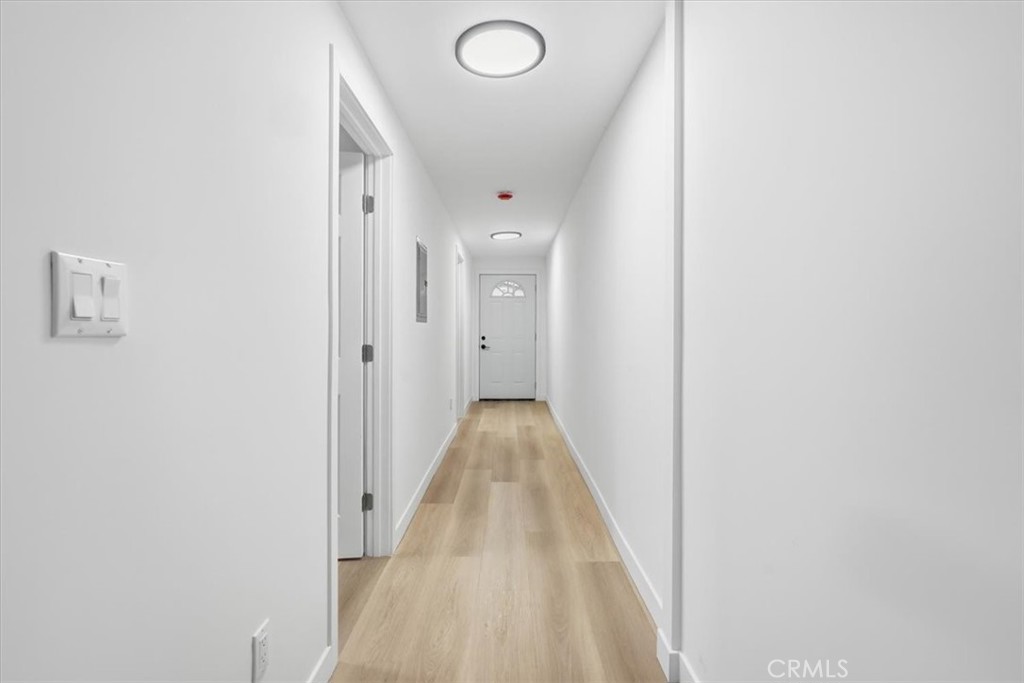 Long white hallway with light wood flooring and a front door with a fanlight window.