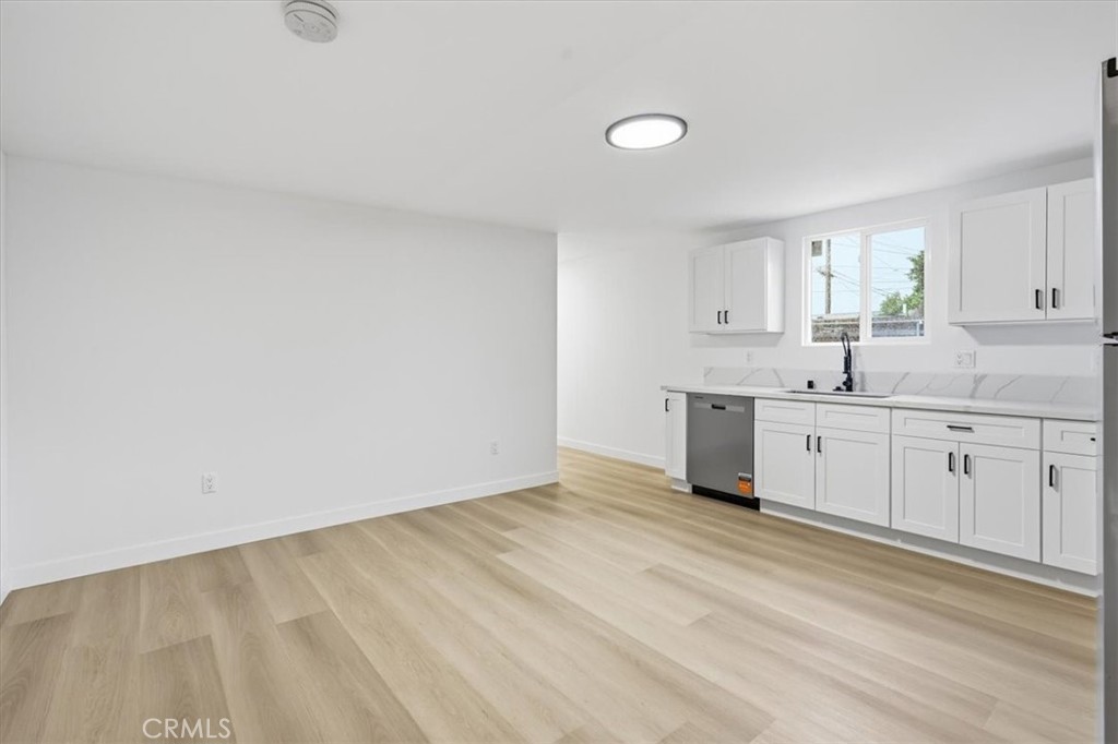 Empty kitchen with white cabinets, a window above the sink, and light wood-look flooring.