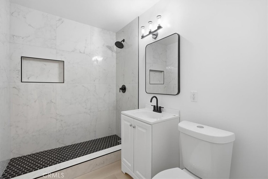 Bathroom with a marble-look walk-in shower, black hexagonal tile floor, and white vanity.
