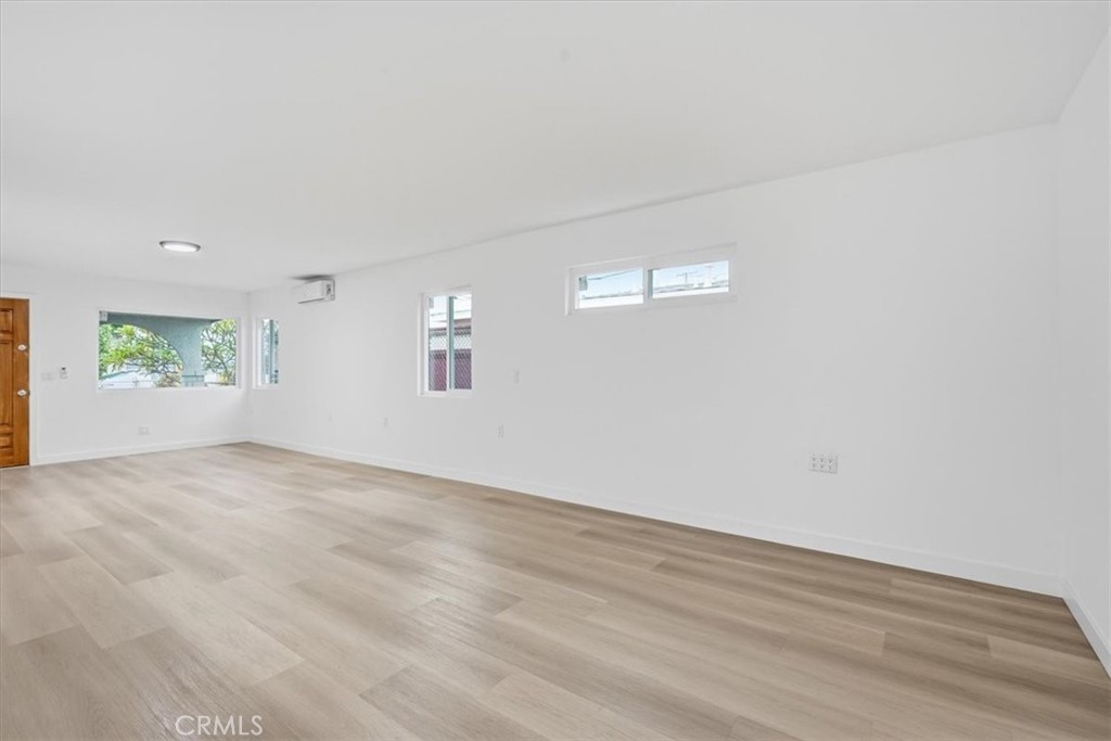 Empty living room with light wood-look flooring, several windows, and a wall-mounted air conditioner.