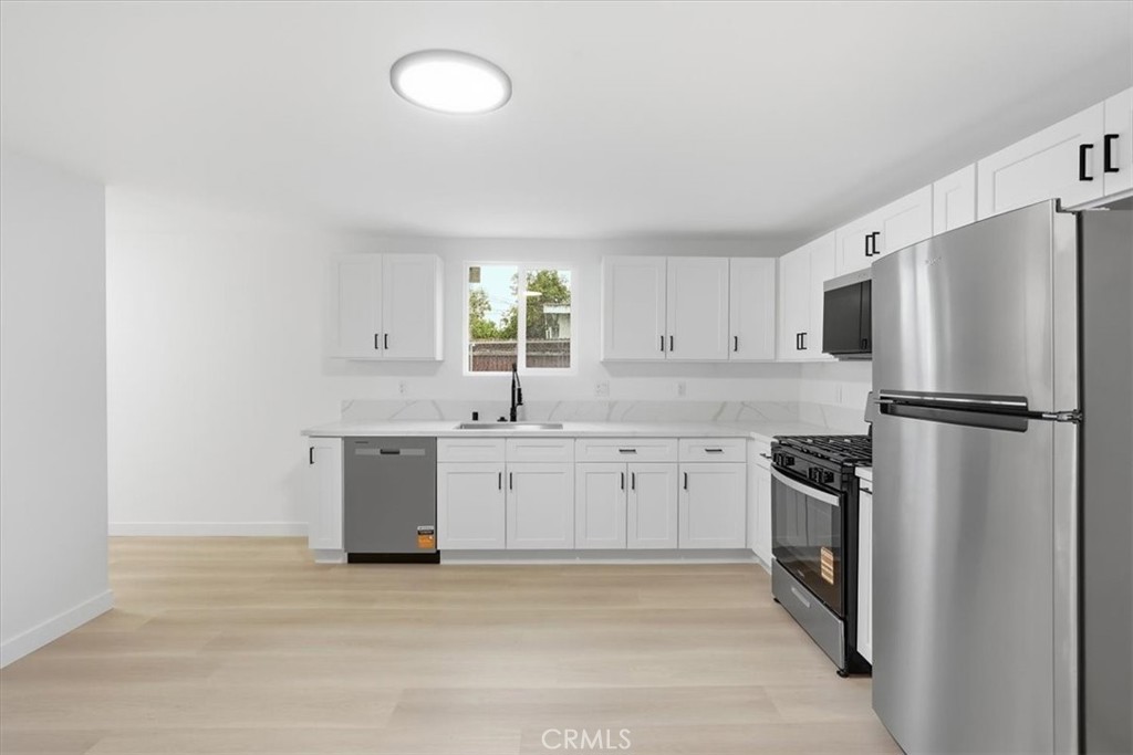 Bright kitchen with white cabinets, stainless steel appliances, and light wood flooring.