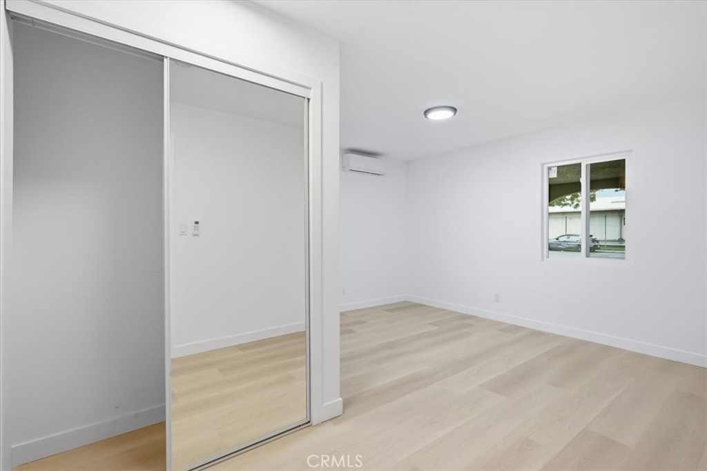 Vacant bedroom with pale wood flooring, mirrored sliding closet doors, and a wall-mounted mini-split.