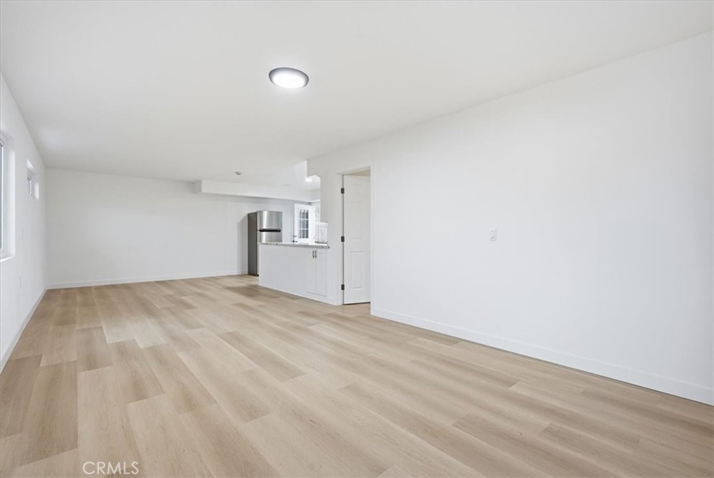 Vacant living area with light wood-look flooring and a compact kitchen at the far end.