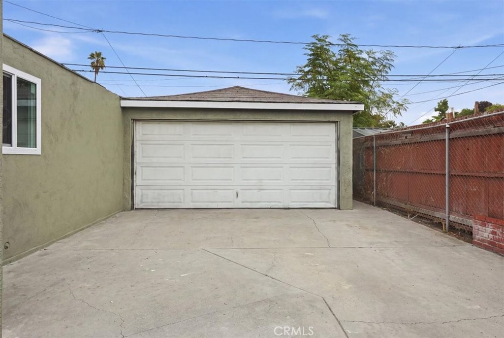 Detached garage with a wide white door and cracked concrete driveway.