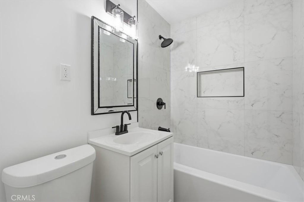 Bathroom with marble-look shower walls, a recessed niche, and a white vanity with black fixtures.