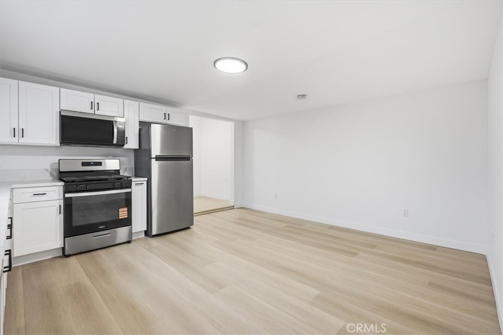 Vacant kitchen with white cabinets, stainless steel appliances, and light wood-look flooring.