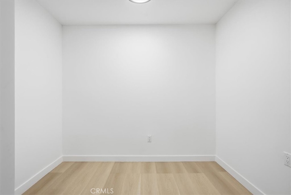 Empty room with light wood flooring, white walls, and a ceiling light.