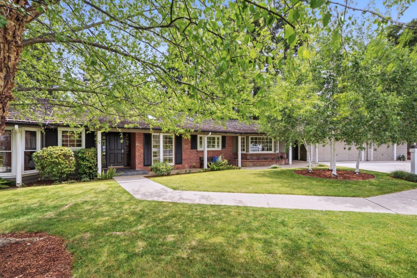 Single-story brick-and-siding home framed by mature trees, with a broad lawn and attached garage.