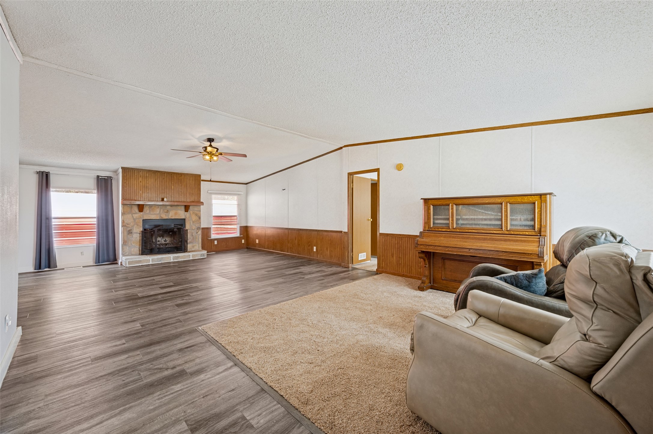 Living room with stone fireplace, wood paneling, upright piano, and a carpeted seating area.