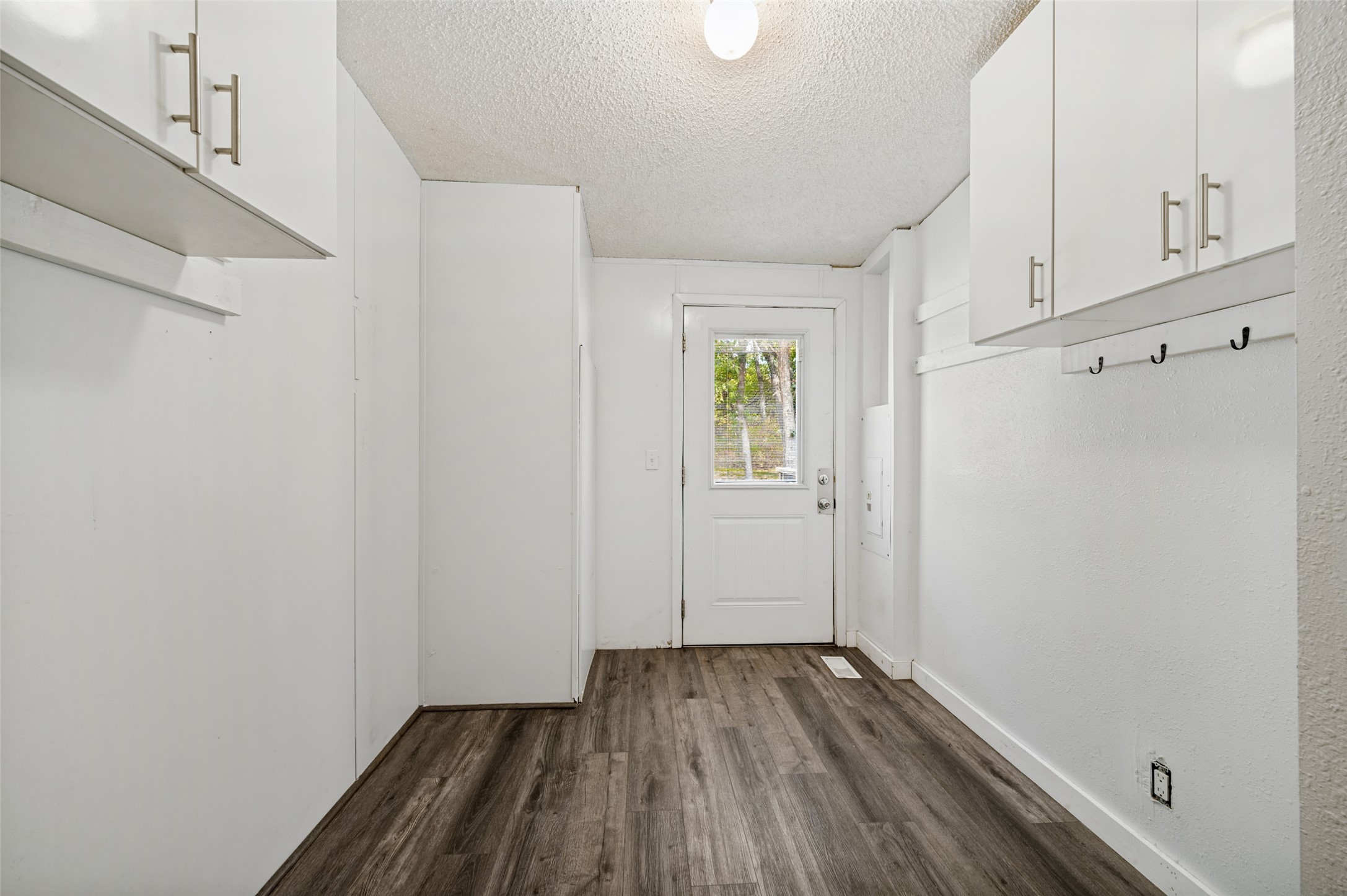 Entryway with white built-in cabinets, coat hooks, dark flooring, and a windowed exterior door.