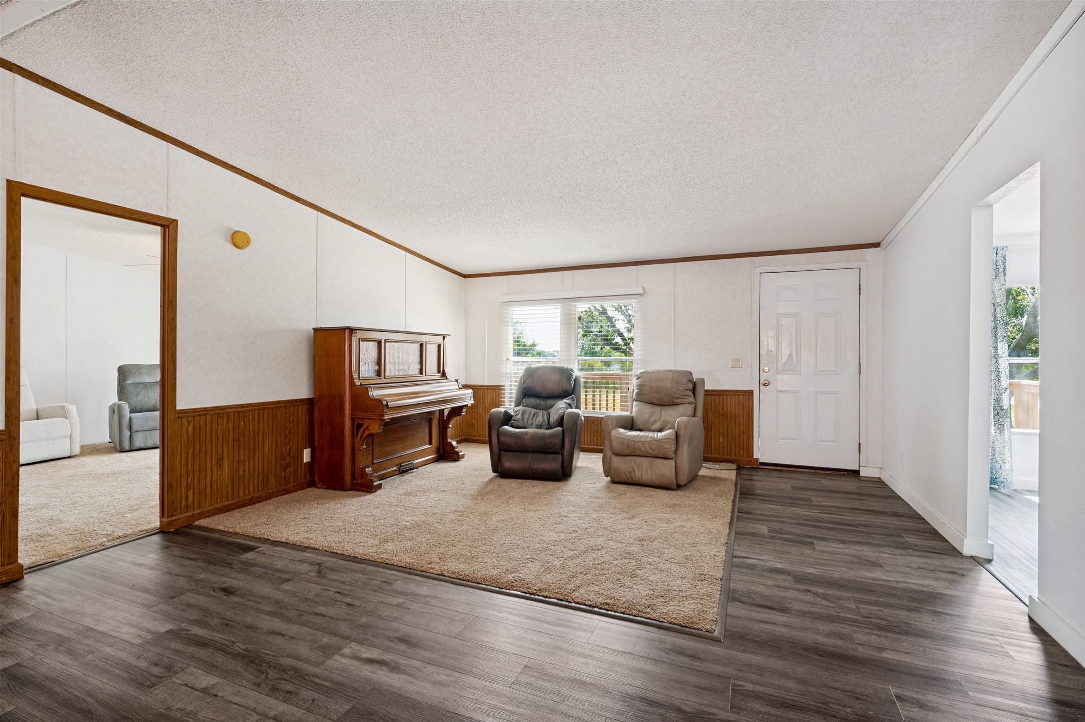 Living room with an upright piano, two recliners, wood-paneled walls, and a carpeted seating area.