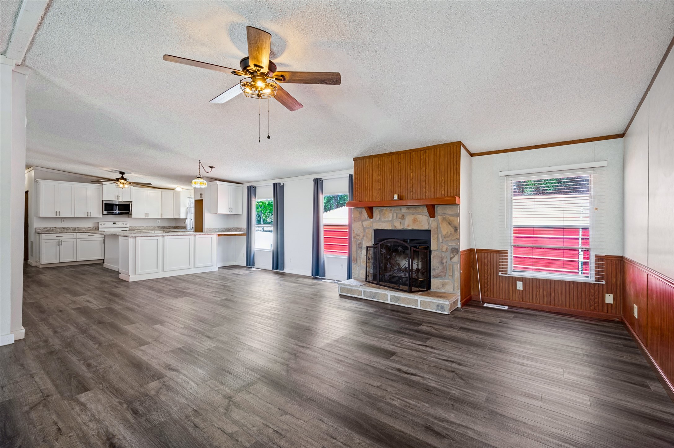 Open living room and kitchen with gray flooring, white cabinets, and a stone fireplace.