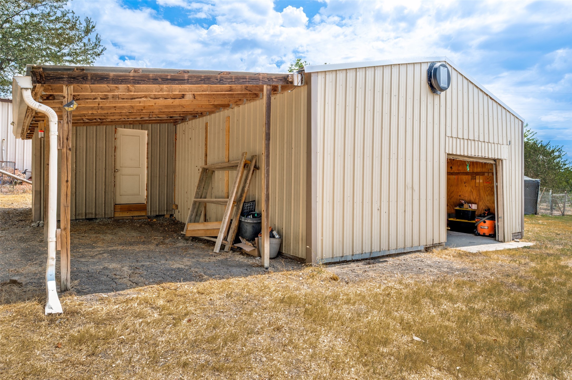 Cream metal workshop with an open equipment bay and a timber-covered work area.