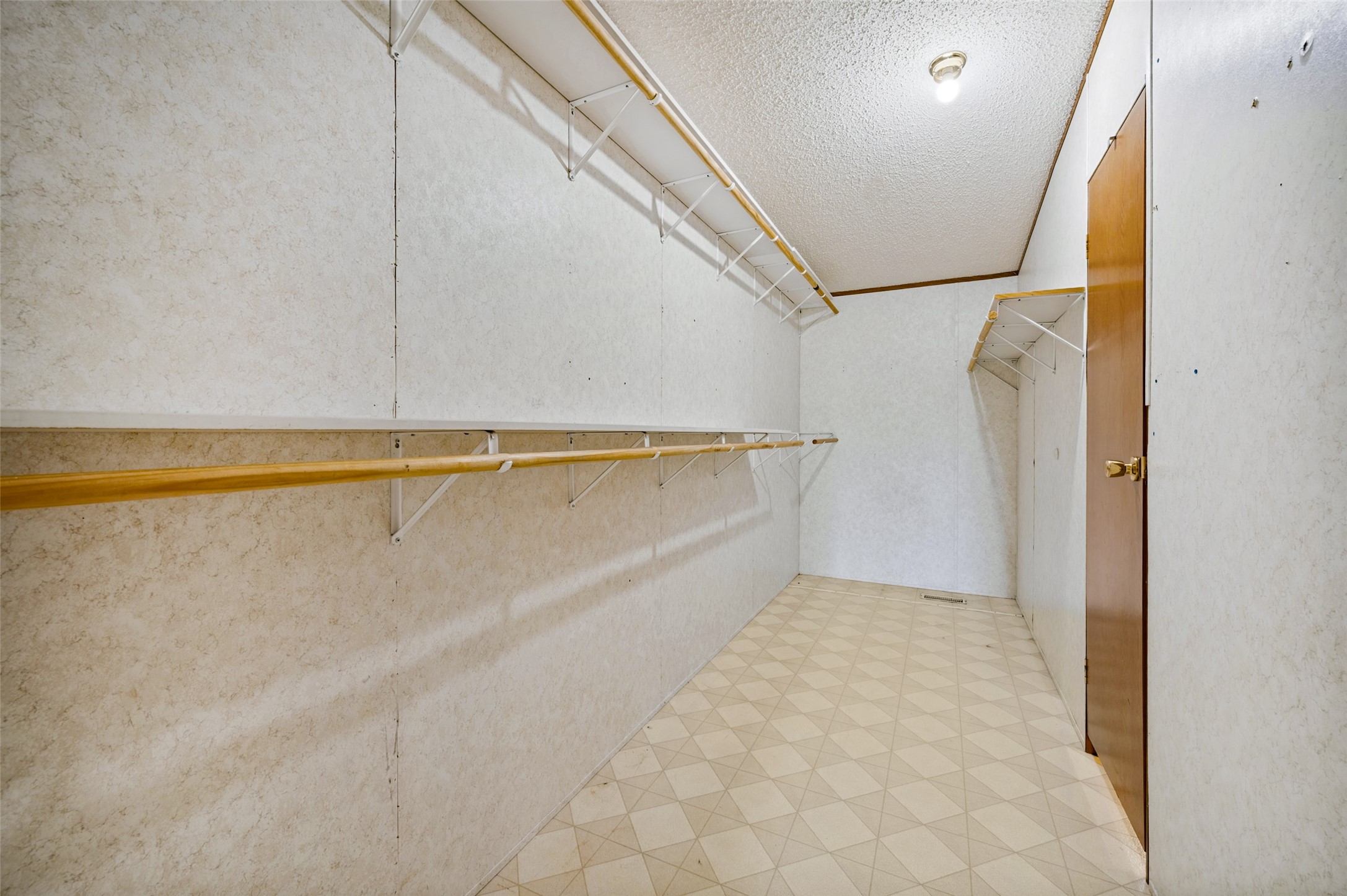 Empty walk-in closet with built-in rods and shelves and patterned tile flooring.
