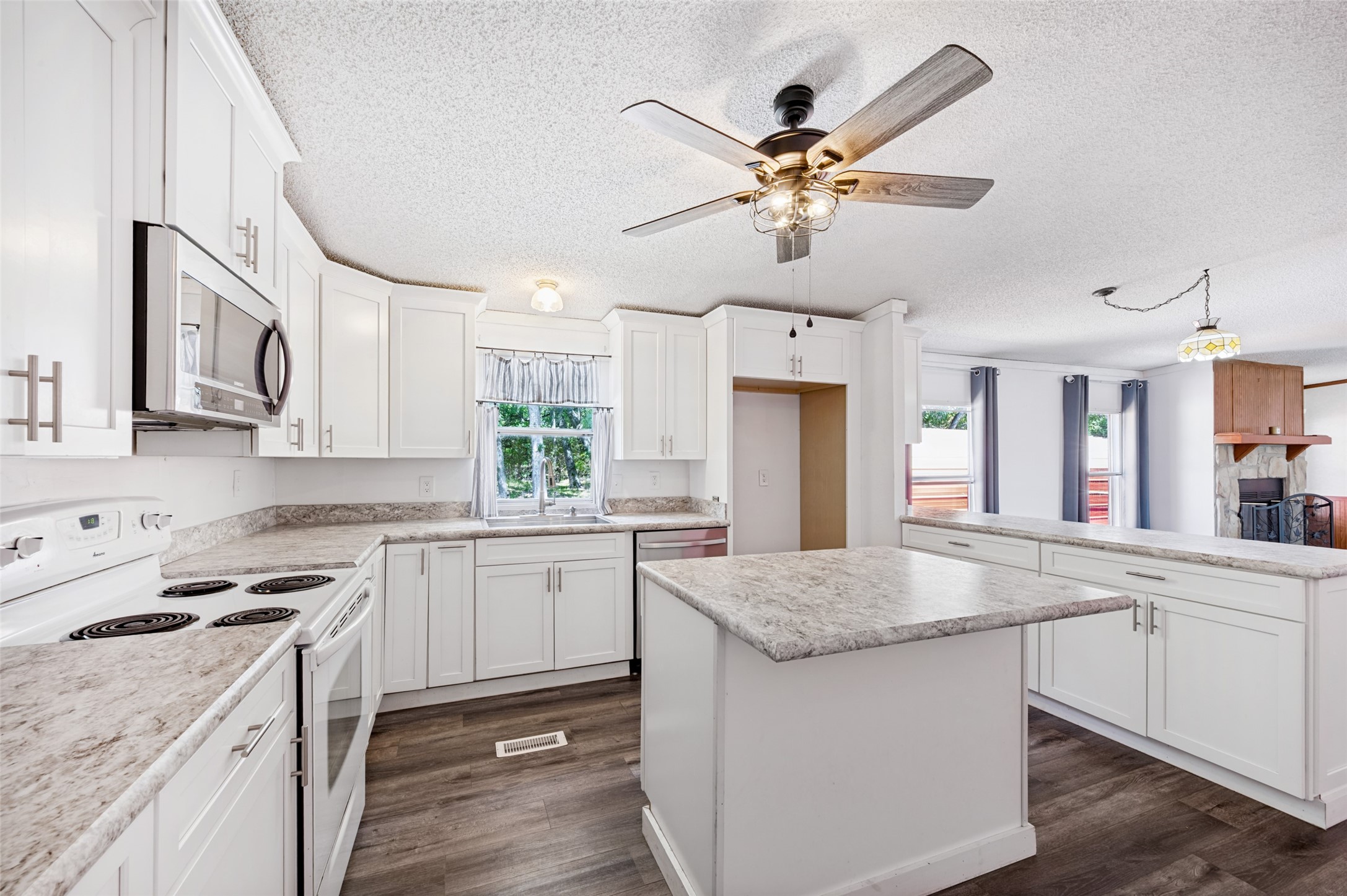 Kitchen with white cabinets, granite countertops, and a large central island; stone fireplace visible beyond.
