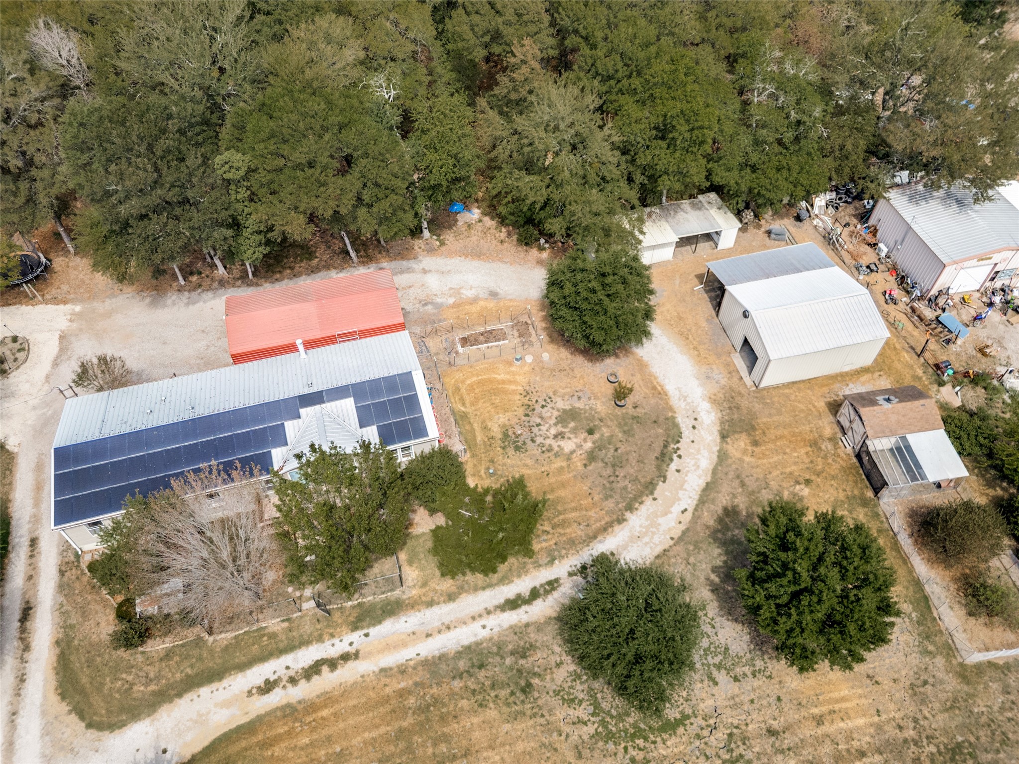 Aerial view of a rural property with solar panels, metal outbuildings, and winding gravel drives.