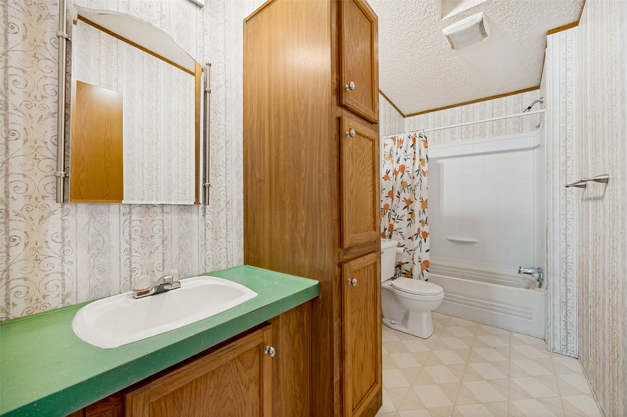 Bathroom with green sink counter, tall wood cabinets, and a tub behind a fruit-print shower curtain.