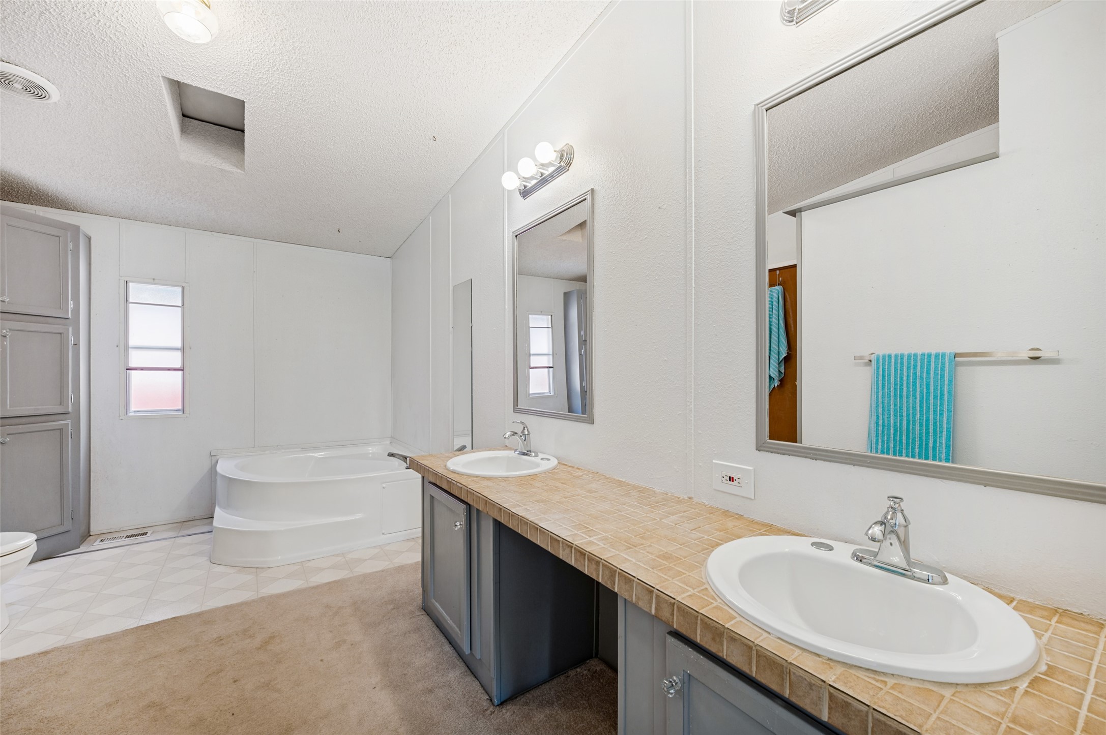 Bathroom with a corner soaking tub, double sinks, tiled countertop, and turquoise towel.