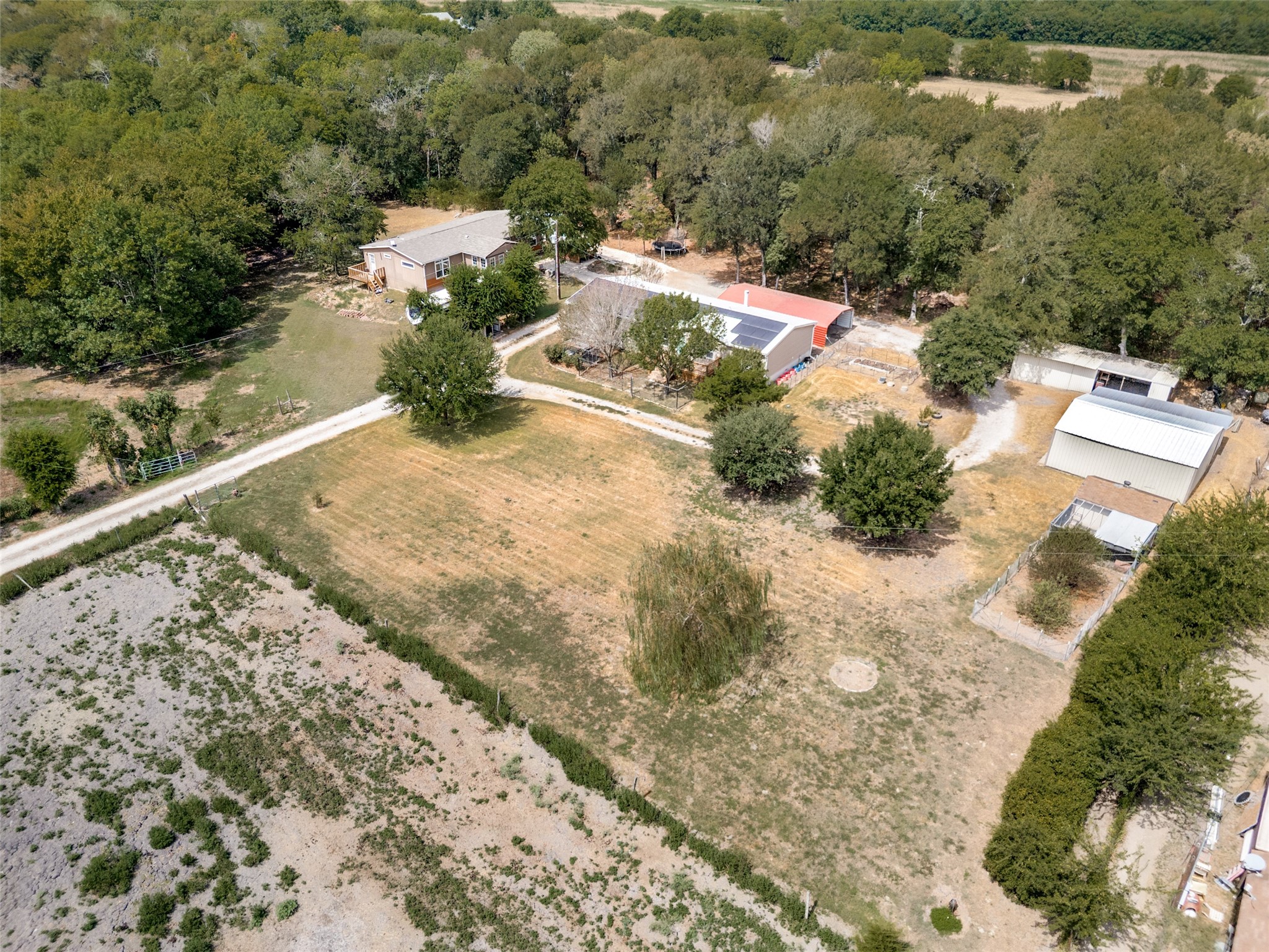 Aerial view of a rural home with solar panels, outbuildings, and a large tree-lined yard.