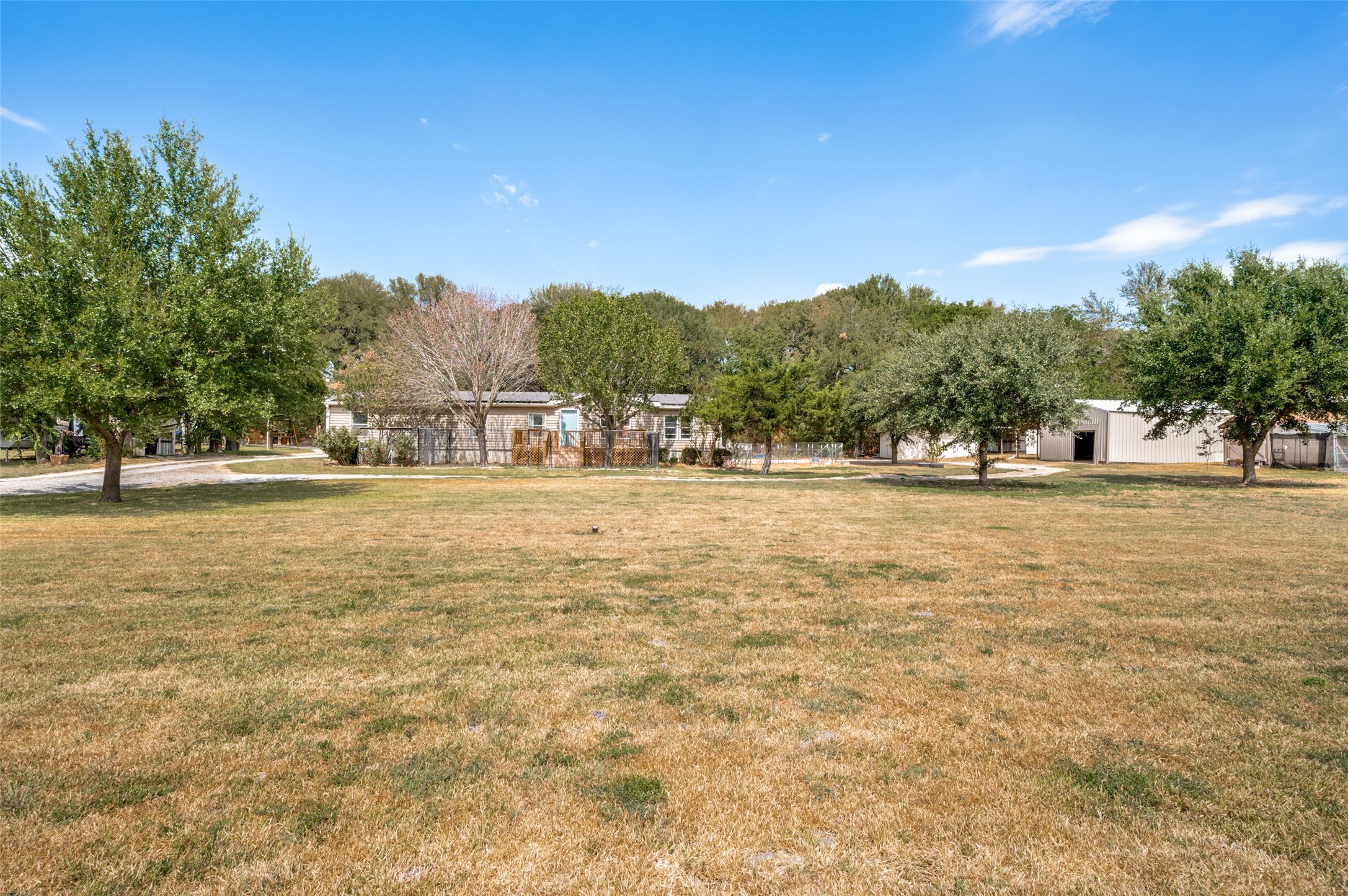 Single-story home and metal outbuilding beyond a broad lawn, framed by mature trees.