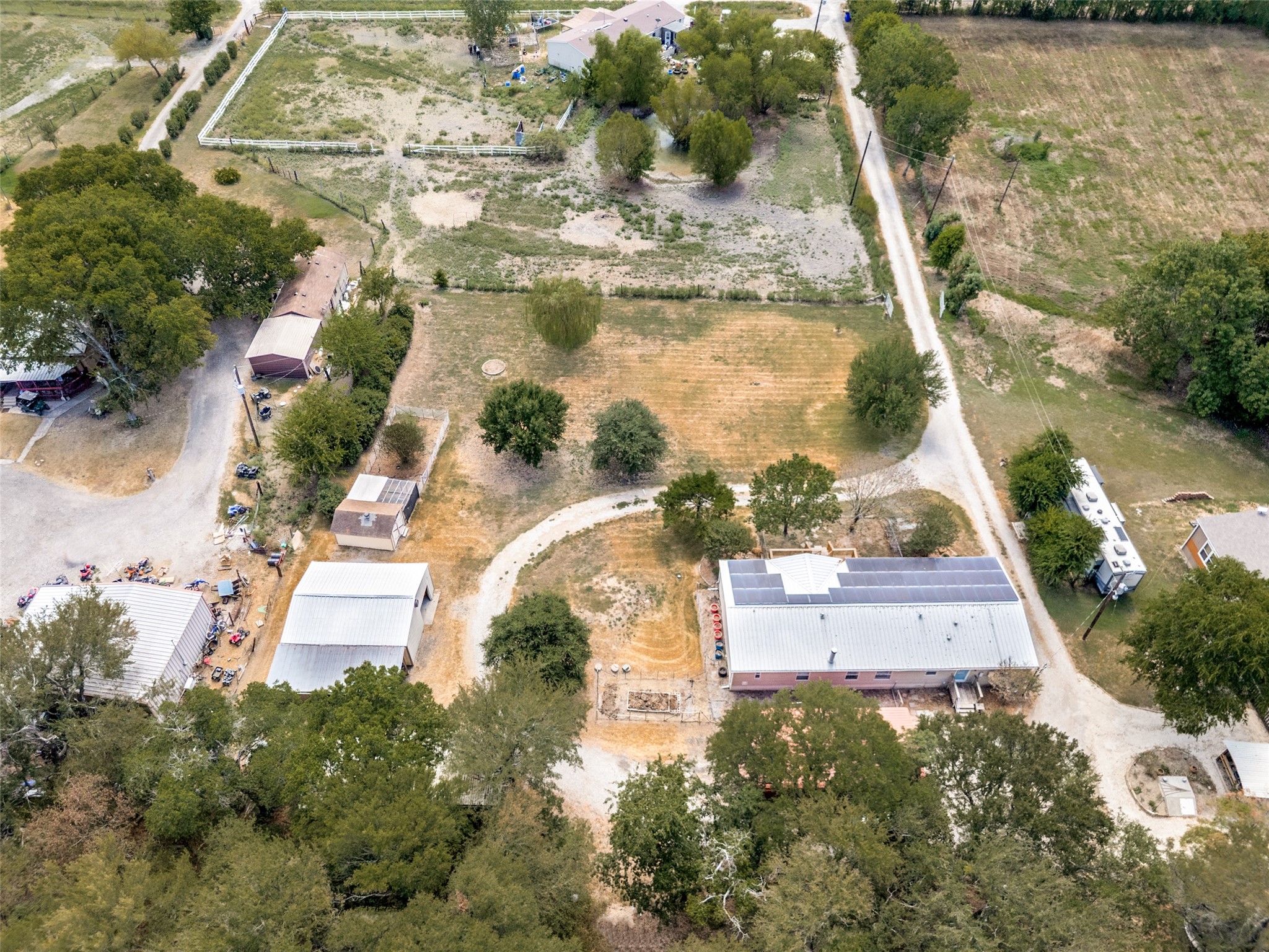 Aerial view of a rural property with solar panels, outbuildings, gravel drives, and mature trees.
