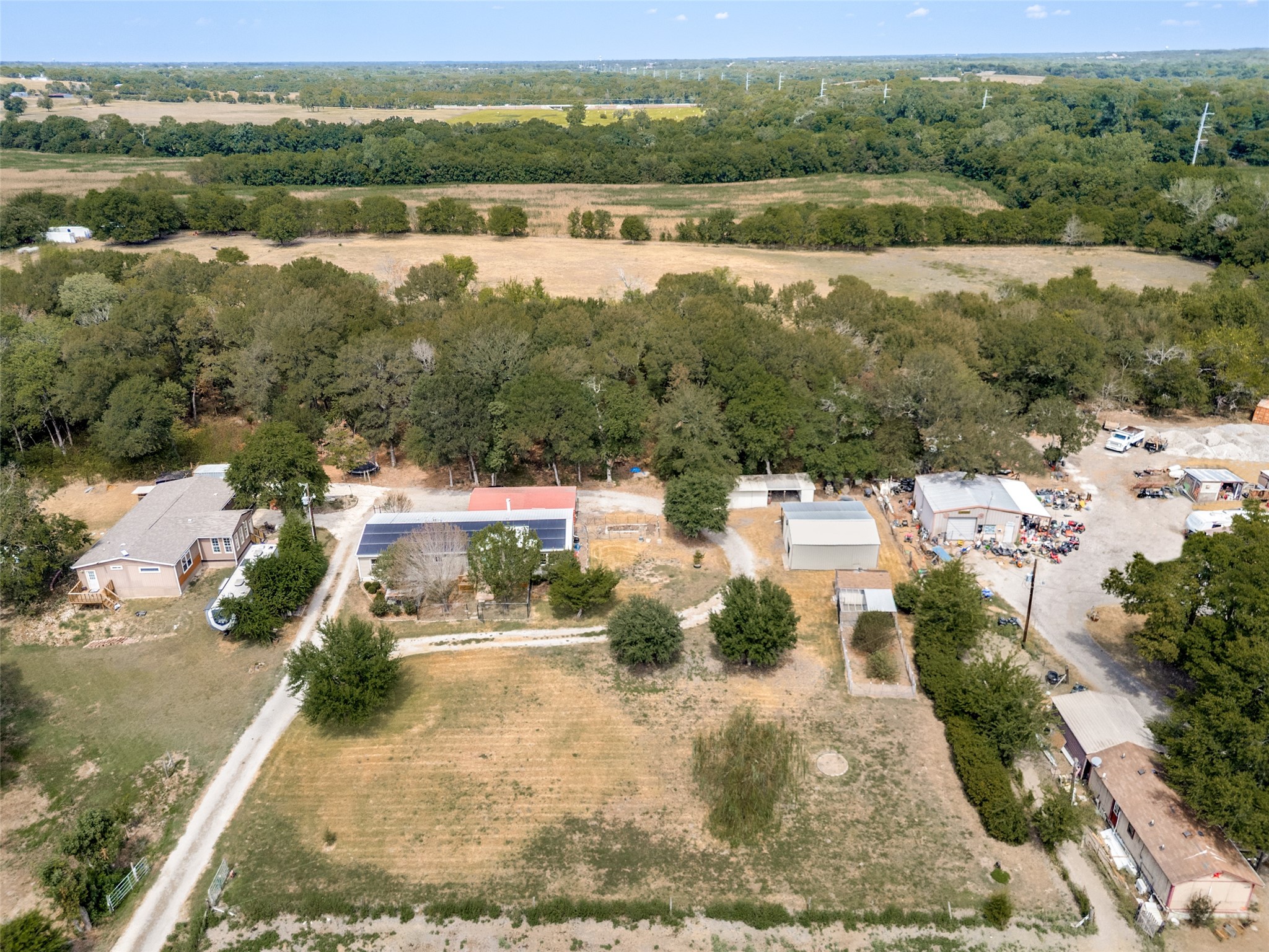 Aerial view of a rural property with homes, outbuildings, solar panels, and surrounding wooded acreage.