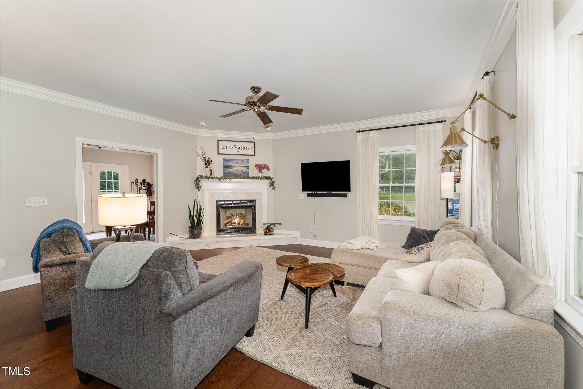Furnished living room with a lit fireplace, sectional seating, and large curtained windows.