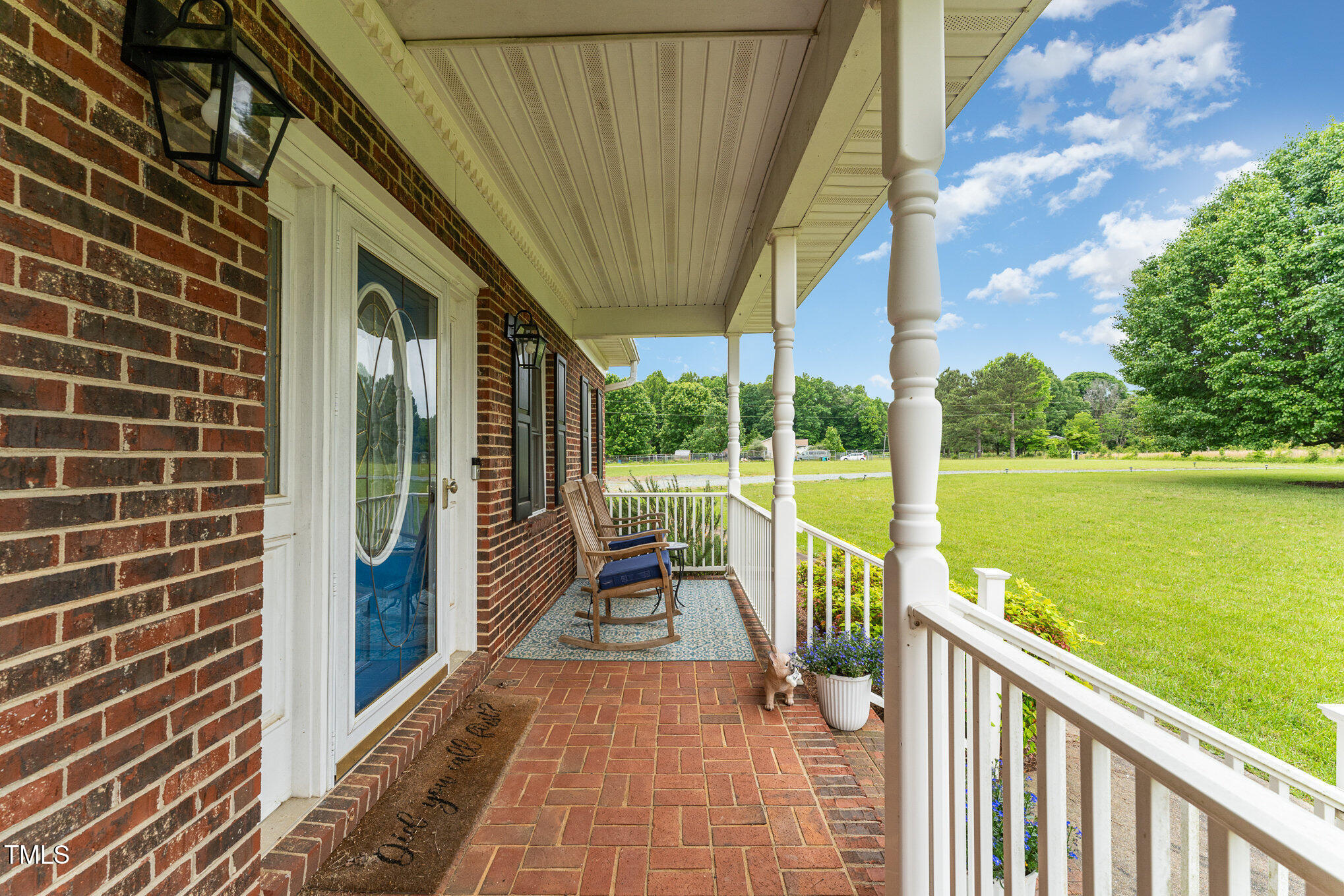 Brick home’s covered front porch with rocking chairs, white columns, and a view across the lawn.